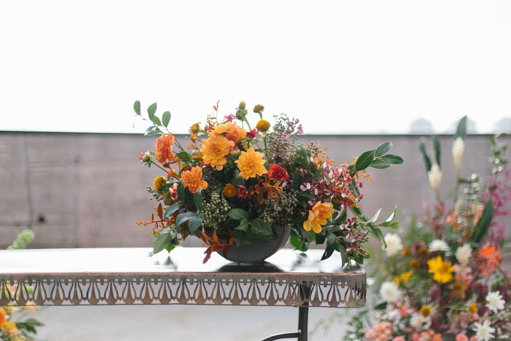 Vibrant orange and yellow floral arrangement on an ornate metal table outdoors.