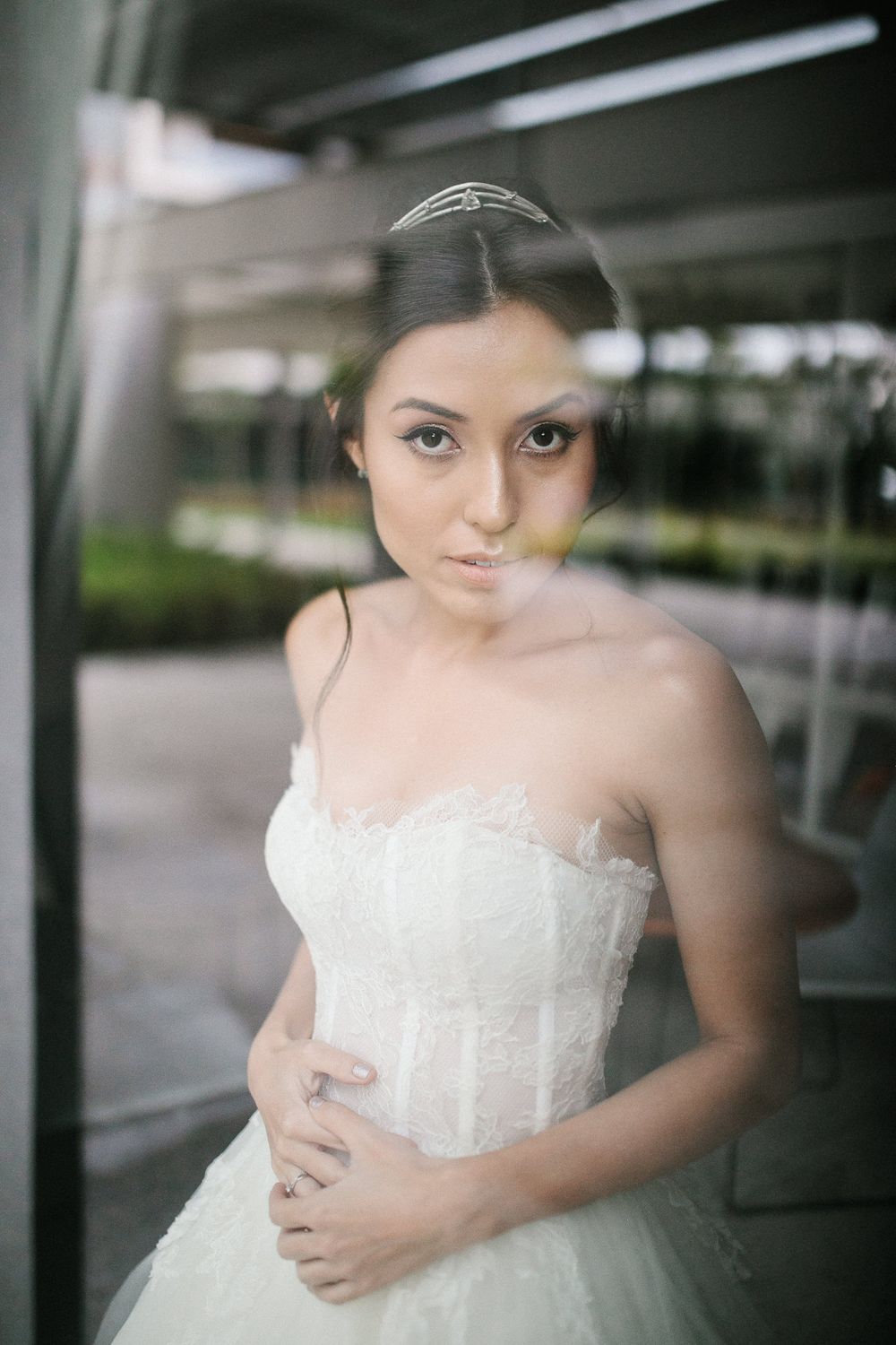 Close-up bridal portrait through glass showing delicate wedding dress details.