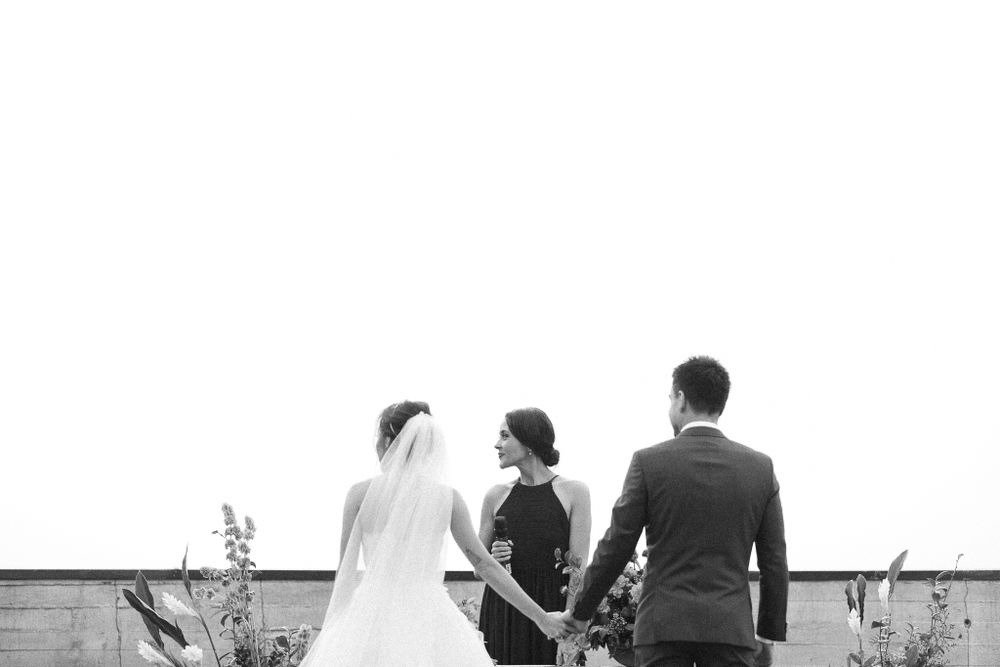 Three wedding attendees stand together on a rooftop overlooking a city skyline.