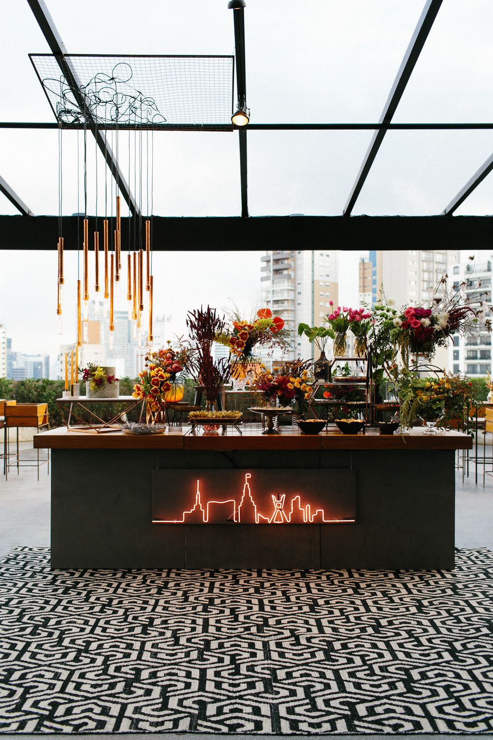 Modern wedding buffet table with neon cityscape sign and geometric patterned floor.