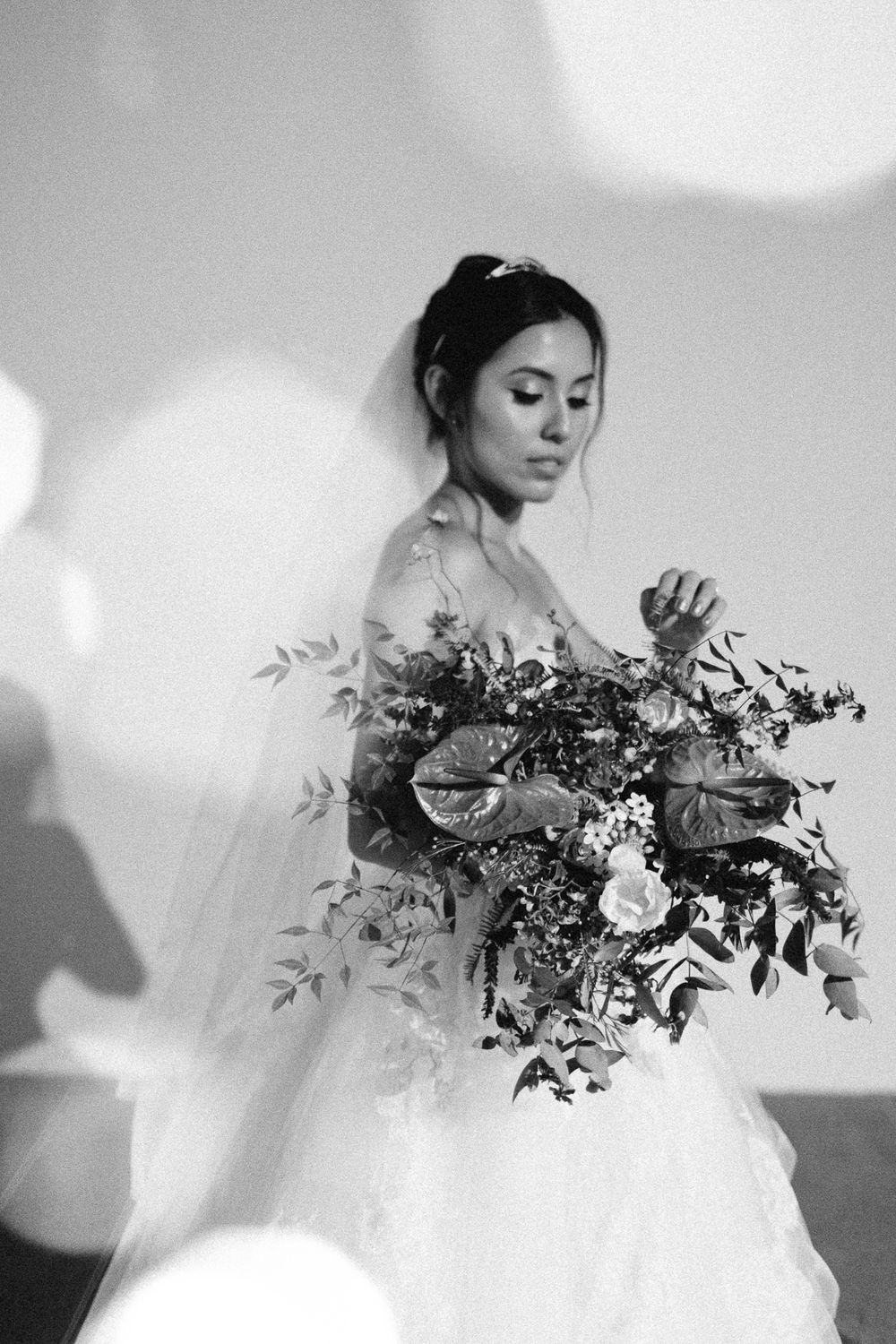 Artistic black and white portrait of bride holding a loose, organic bouquet with dreamy lighting effects.