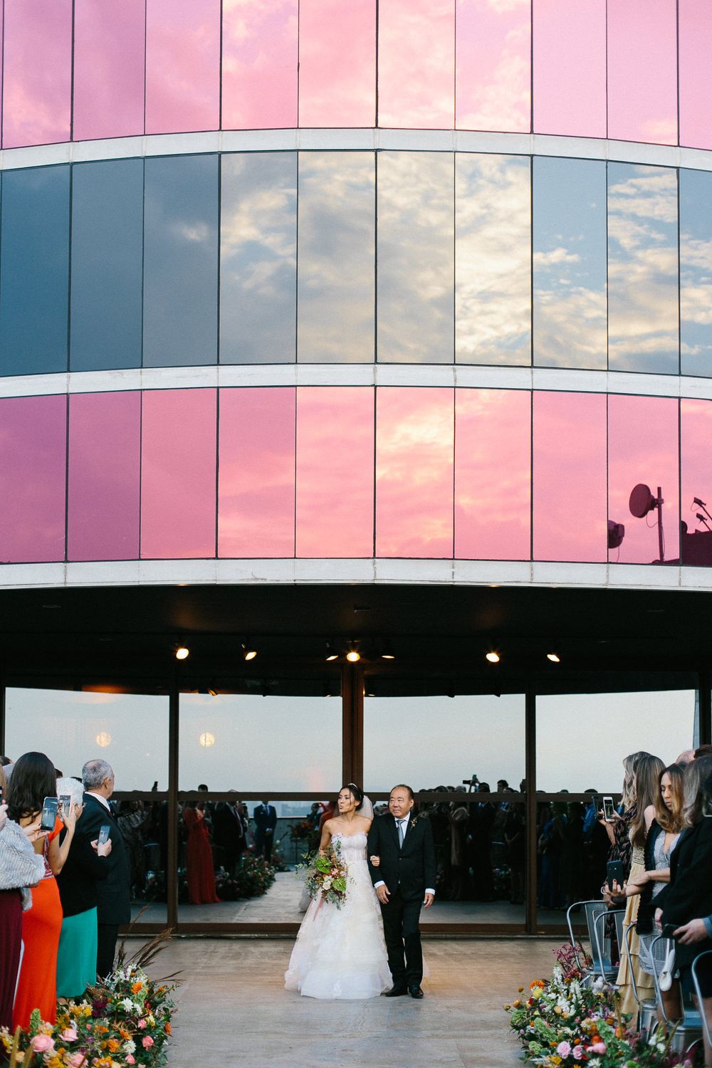 Modern building exterior with pink and reflective glass panels capturing sunset skies.