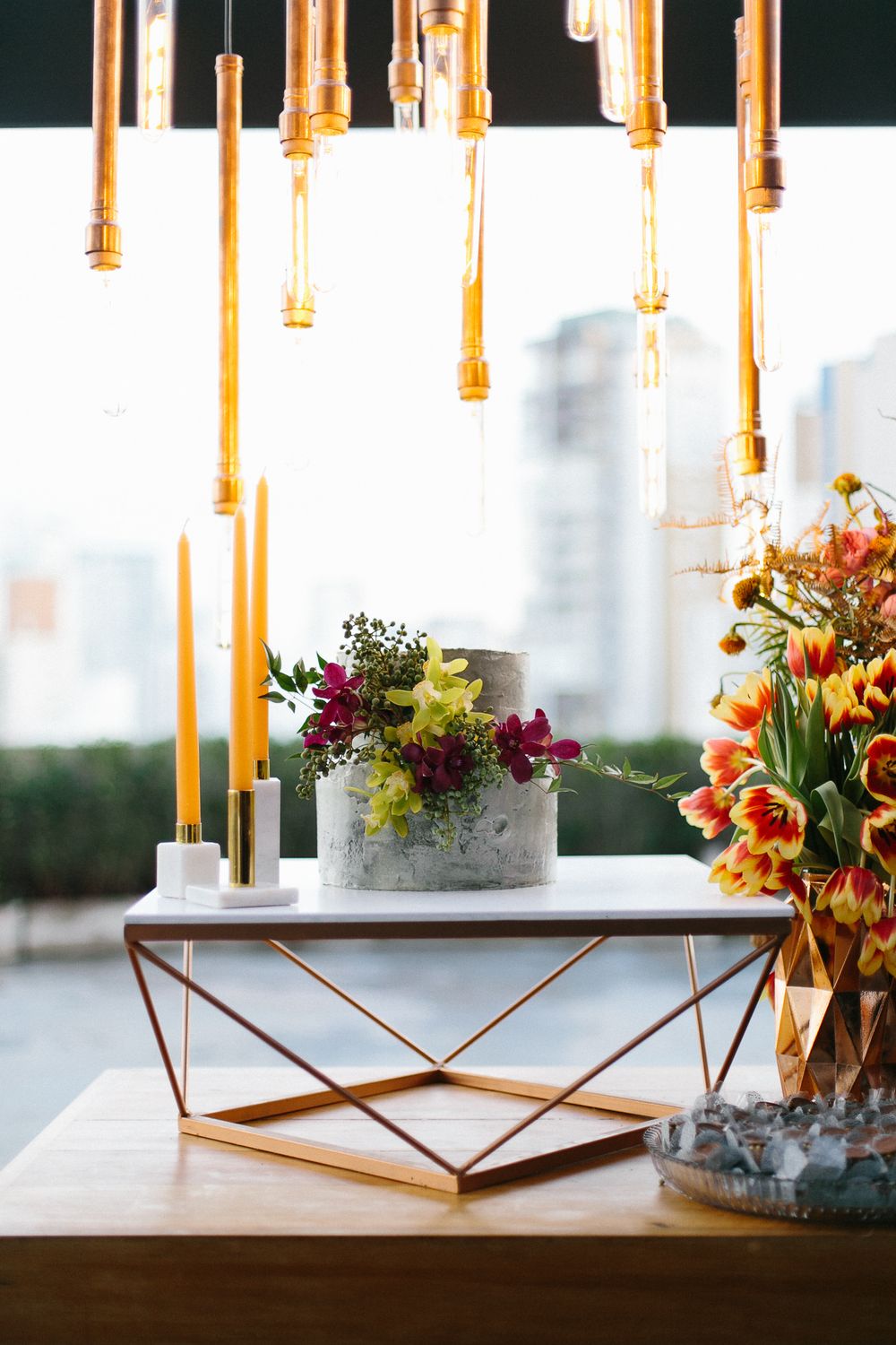 Stylish geometric coffee table with hanging pendant lights and floral arrangements.