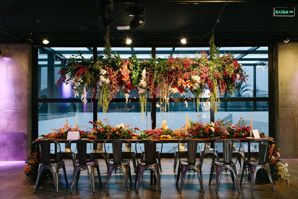 Modern reception table setup with hanging floral installations and industrial metal chairs.