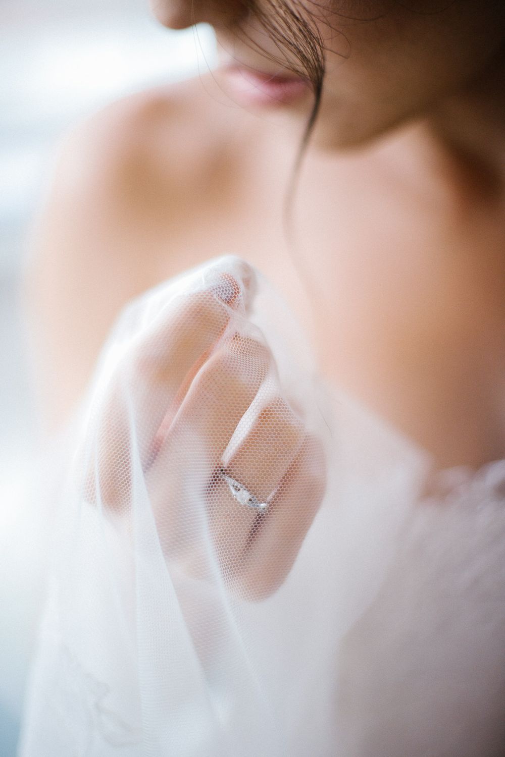 Close-up of a diamond engagement ring through delicate white tulle fabric.