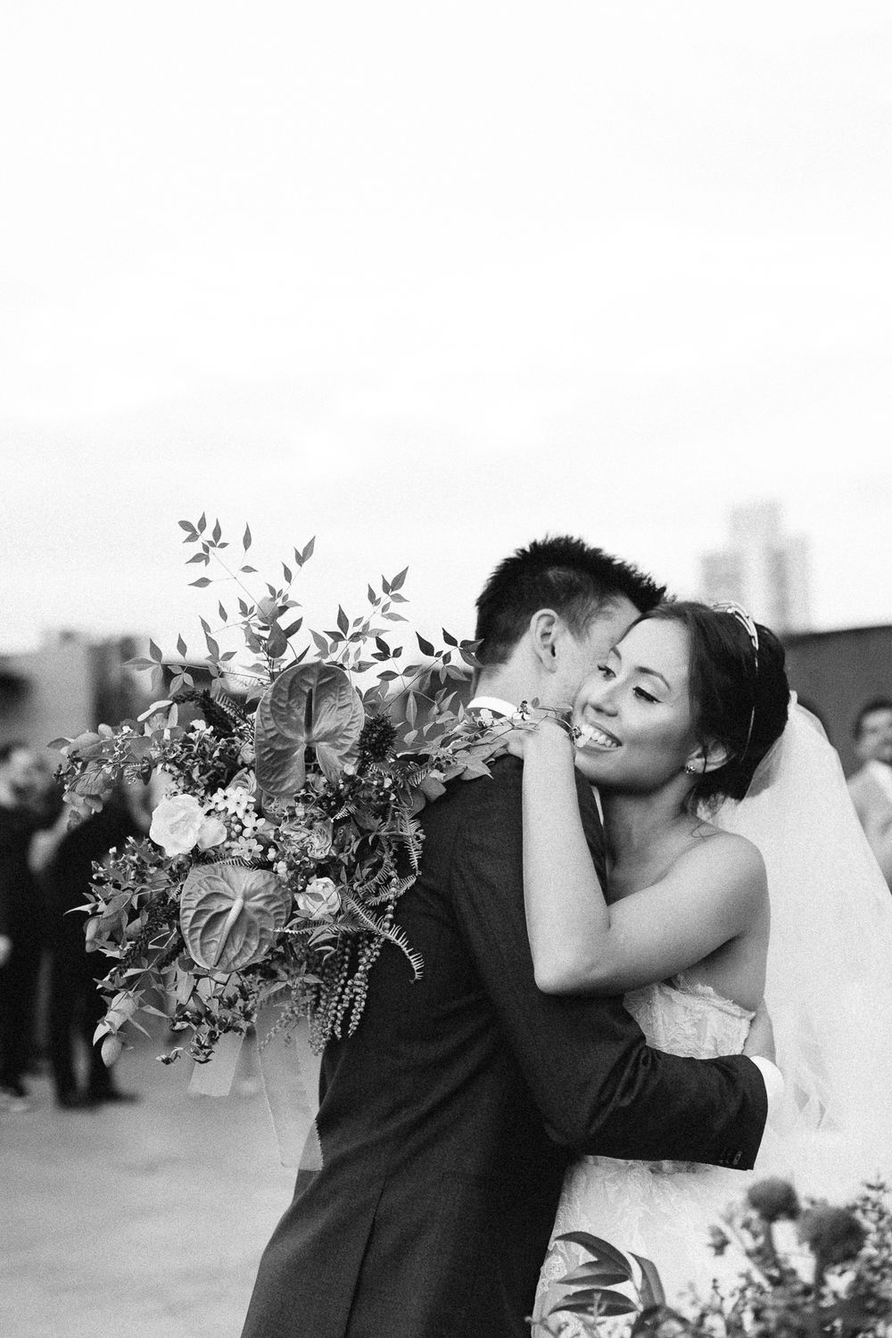 A wedding couple shares an intimate moment with the bride holding a lush floral bouquet in black and white.