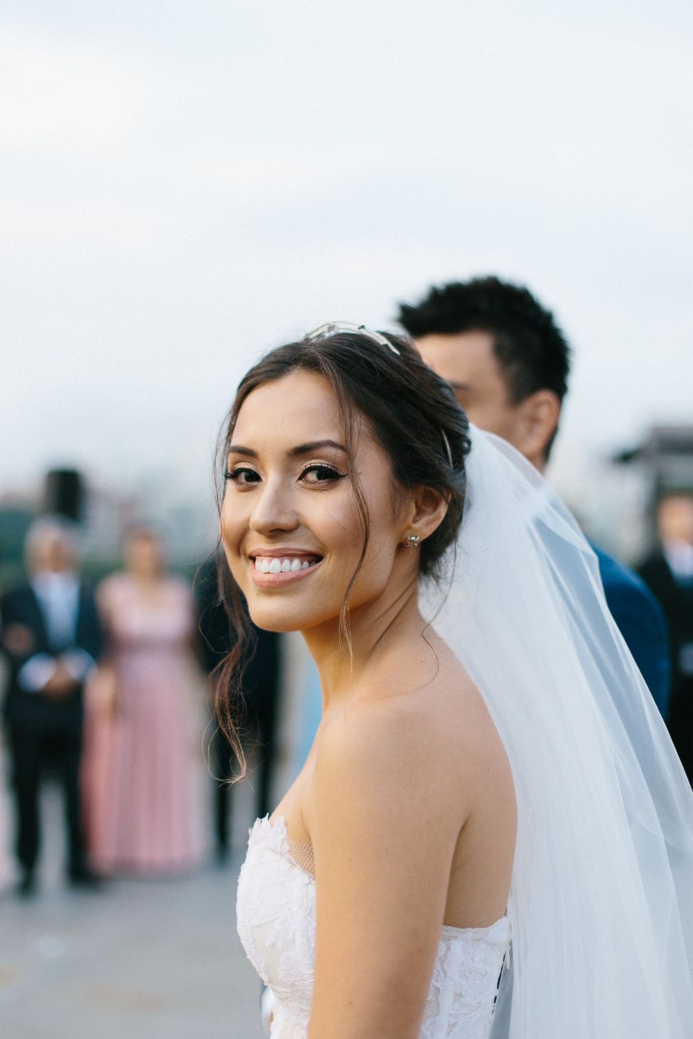 A bride in a white strapless gown and veil smiles radiantly during her wedding day.