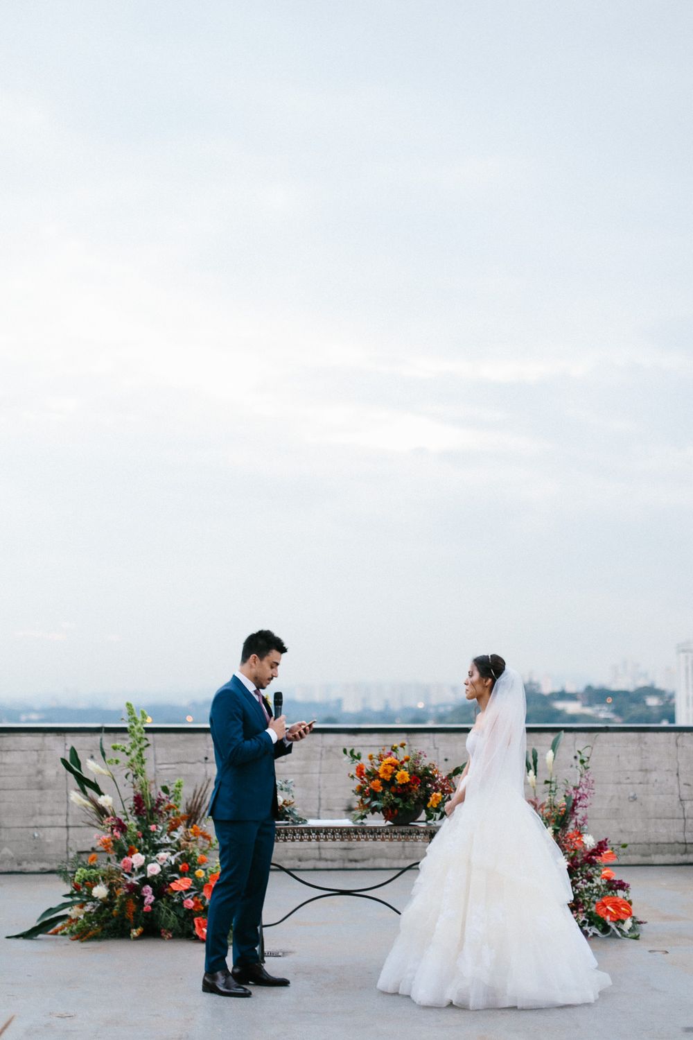 A couple exchanges vows during their rooftop wedding ceremony with vibrant floral arrangements.