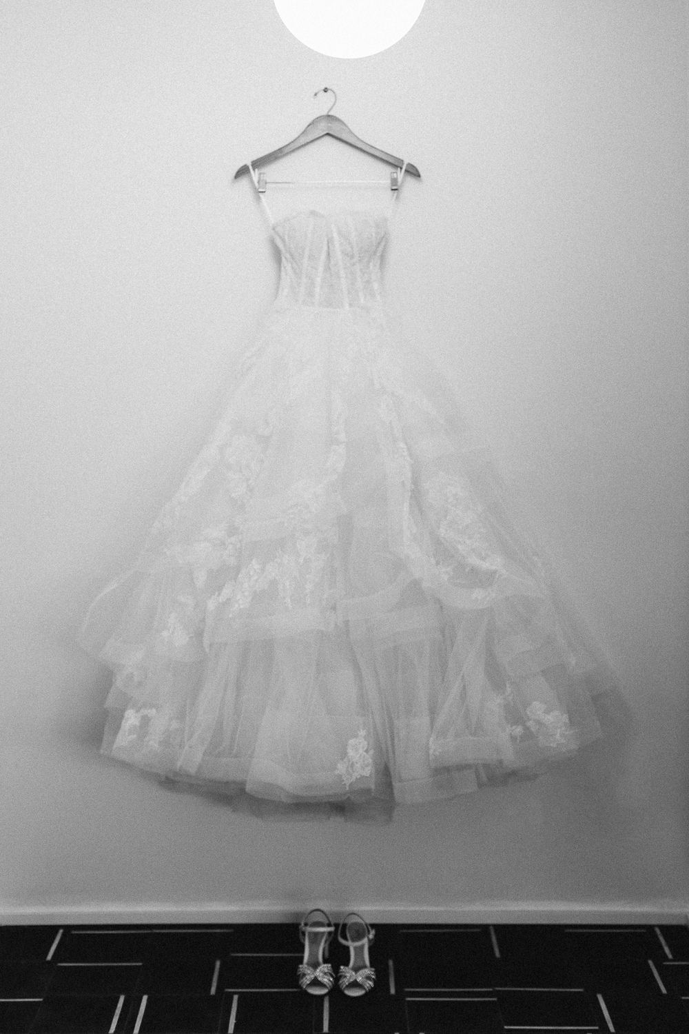 White wedding dress hanging on display with shoes beneath in black and white photography.
