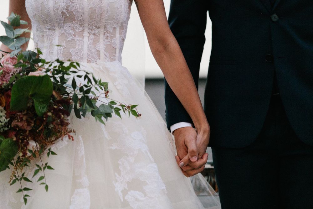 Close-up of bride and groom holding hands, showing white wedding dress and black suit details.