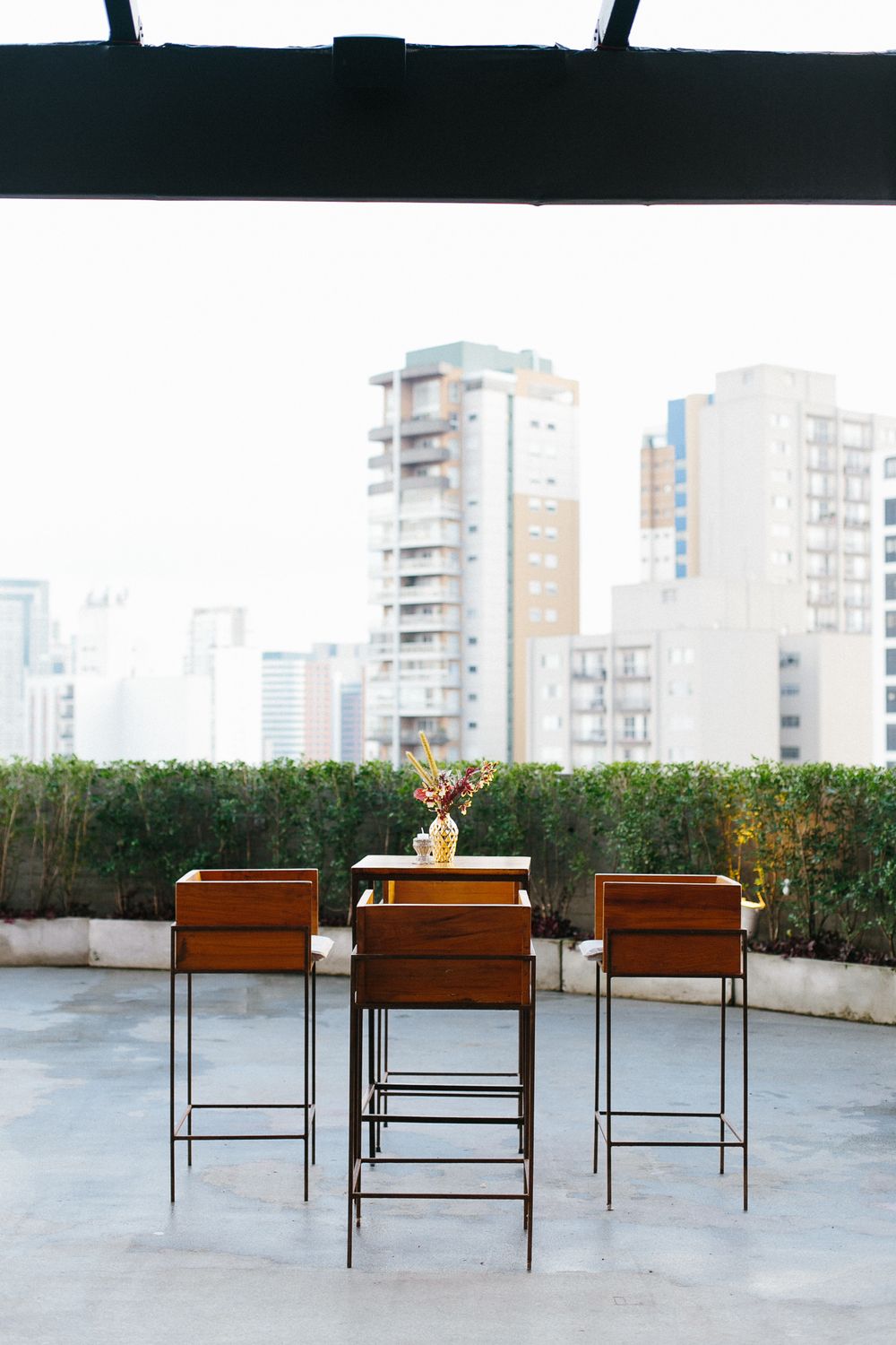 Minimalist rooftop bar setup with three high chairs against city skyline backdrop.