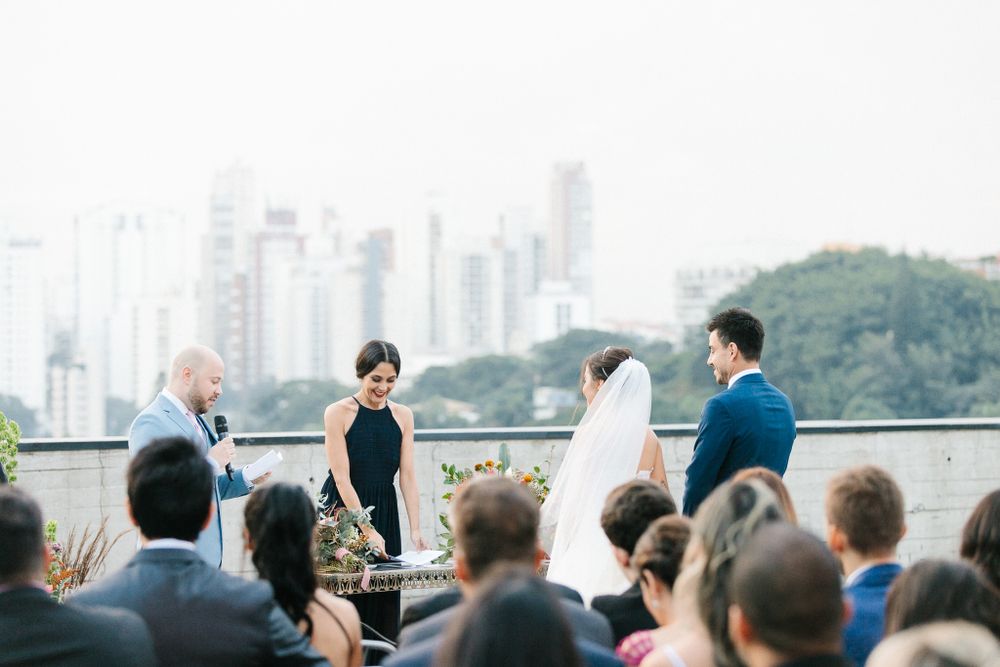 An outdoor wedding ceremony overlooking a city skyline with guests watching the couple exchange vows.