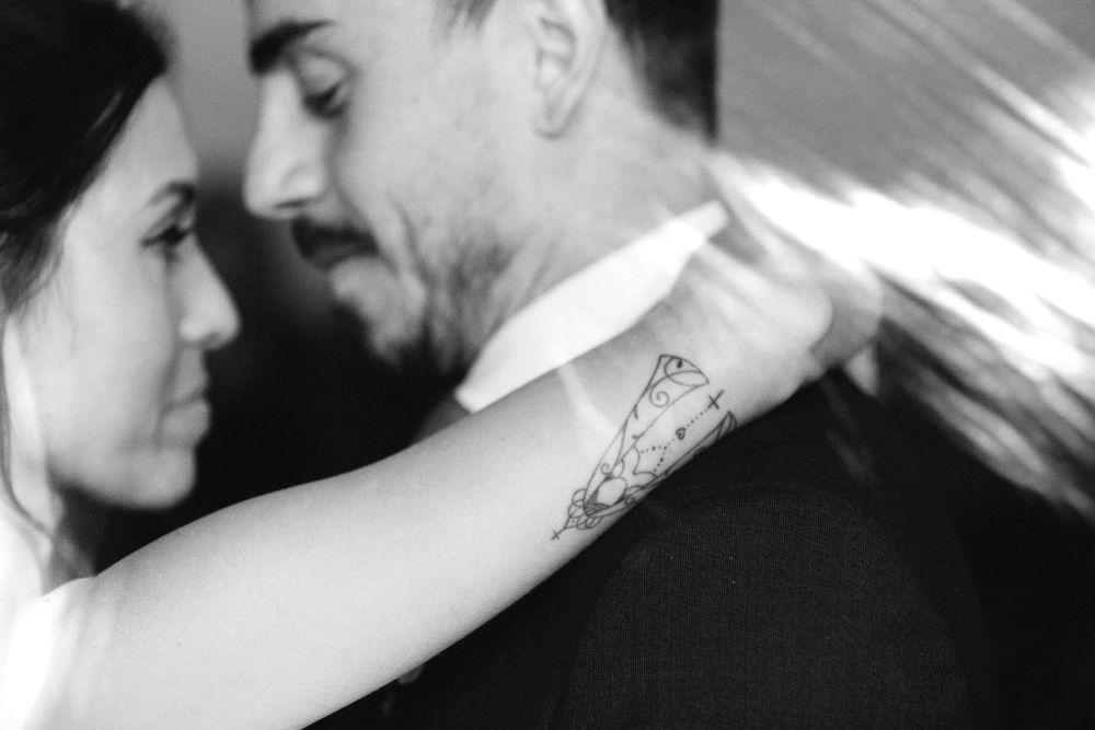 Black and white close-up of a tender wedding dance moment showing the bride's arm with a delicate tattoo.