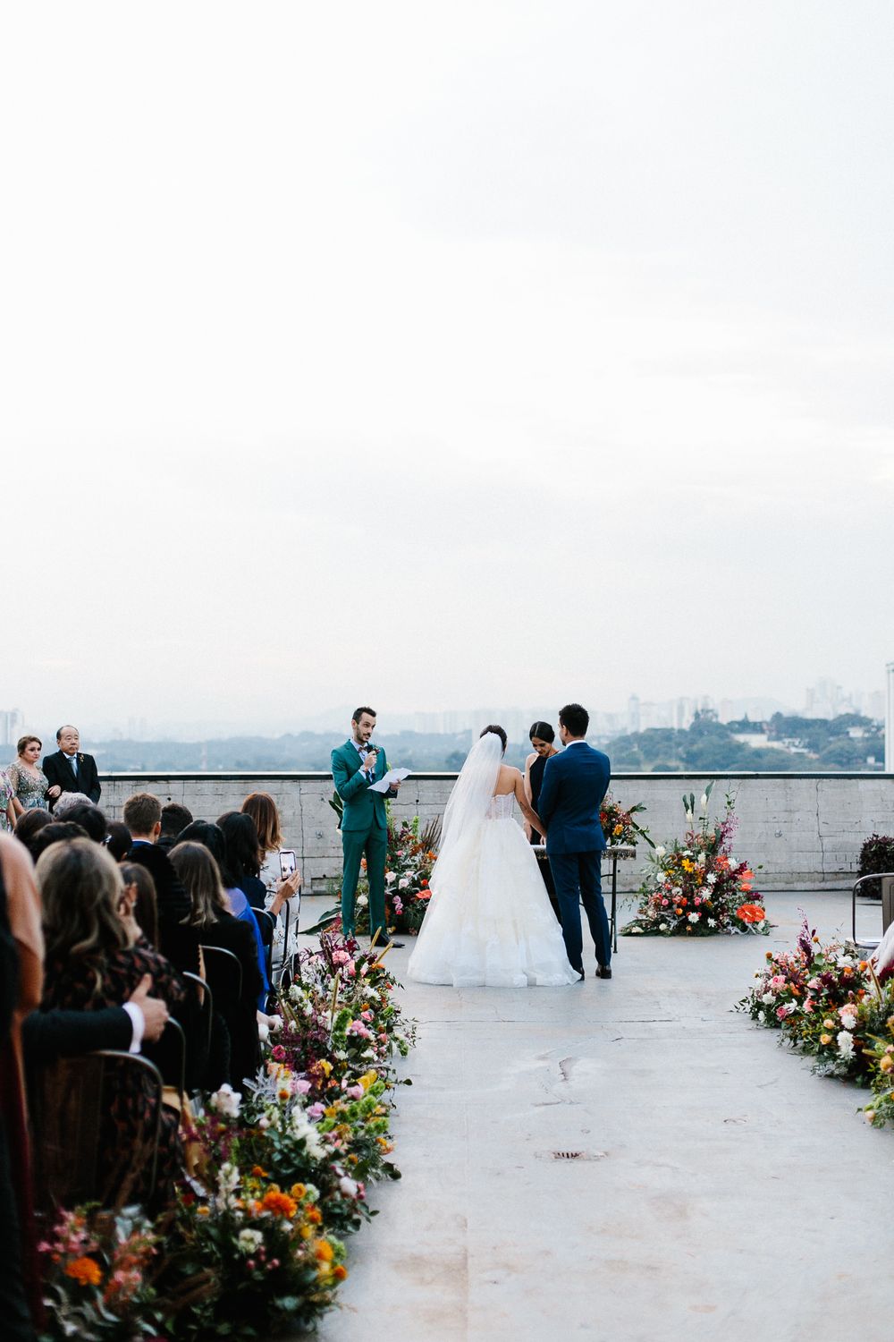 A rooftop wedding ceremony setup with colorful floral arrangements and guests seated facing the cityscape.