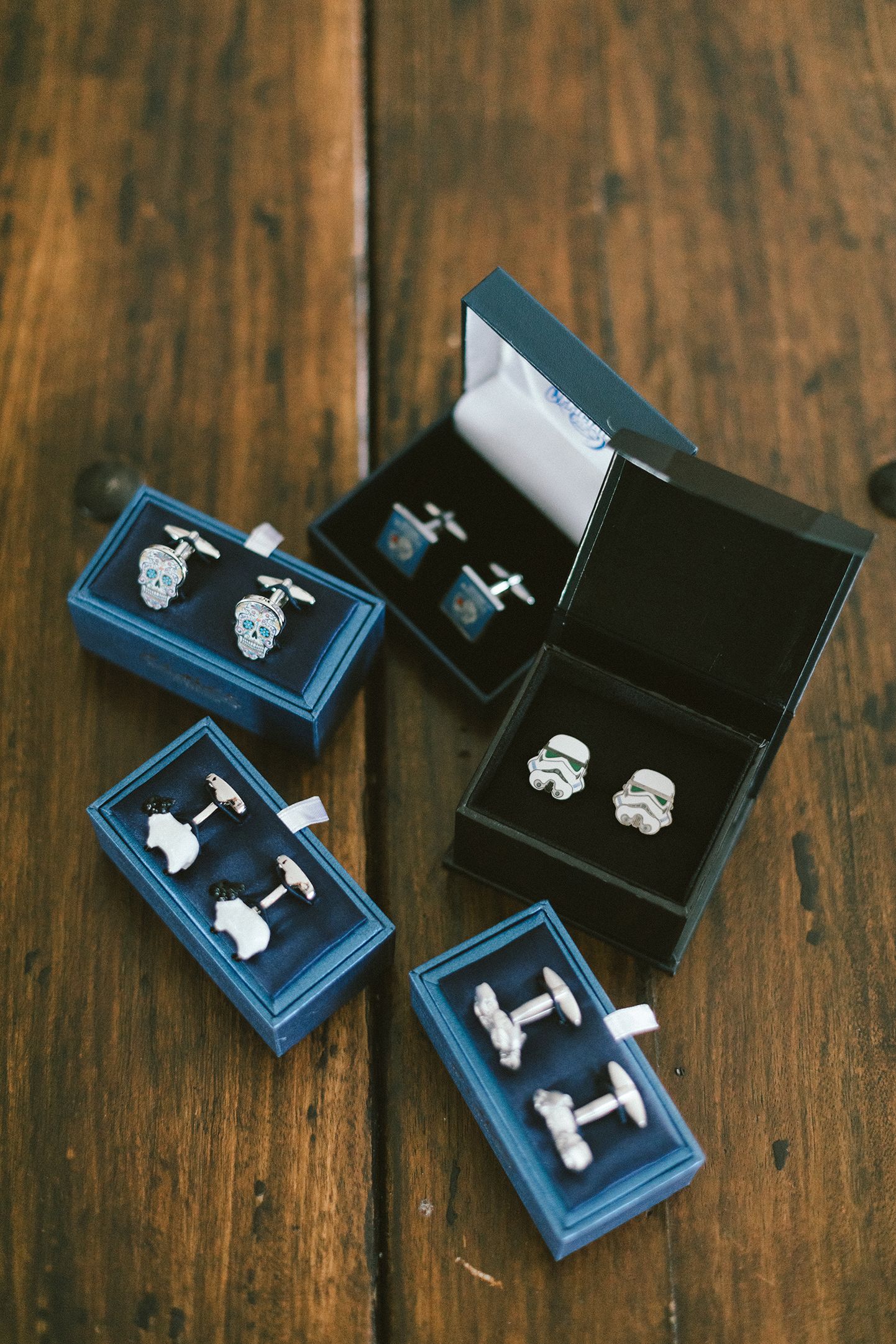 Collection of cufflinks displayed in blue and black gift boxes on wooden surface.