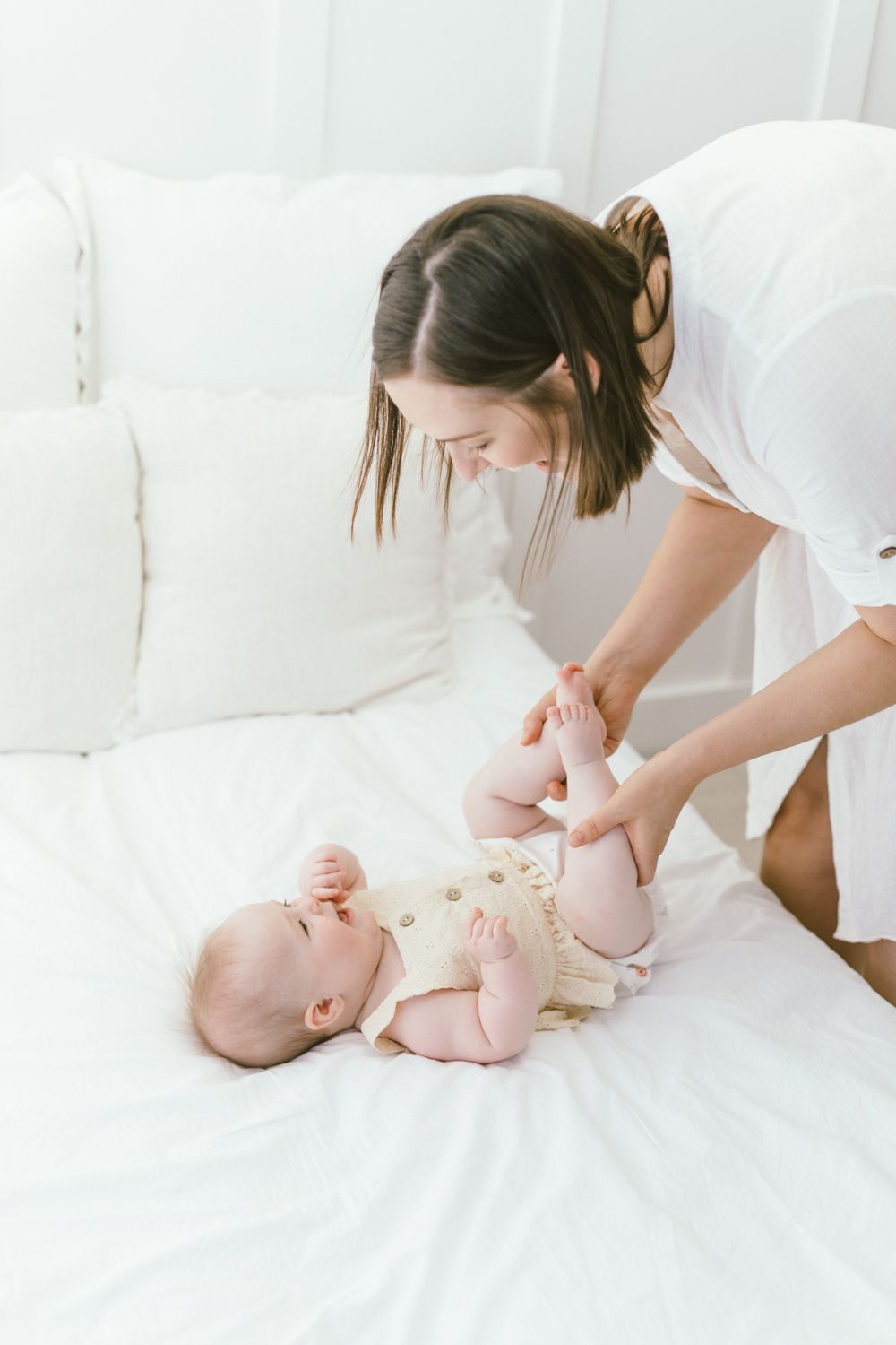 Caregiver engaging with infant during playful moment on white couch.