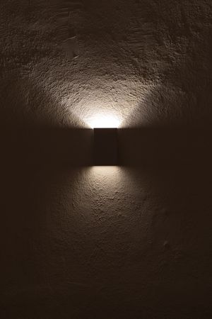 Modern wall sconce creates dramatic up and down lighting effect on textured brown wall surface in dark room.