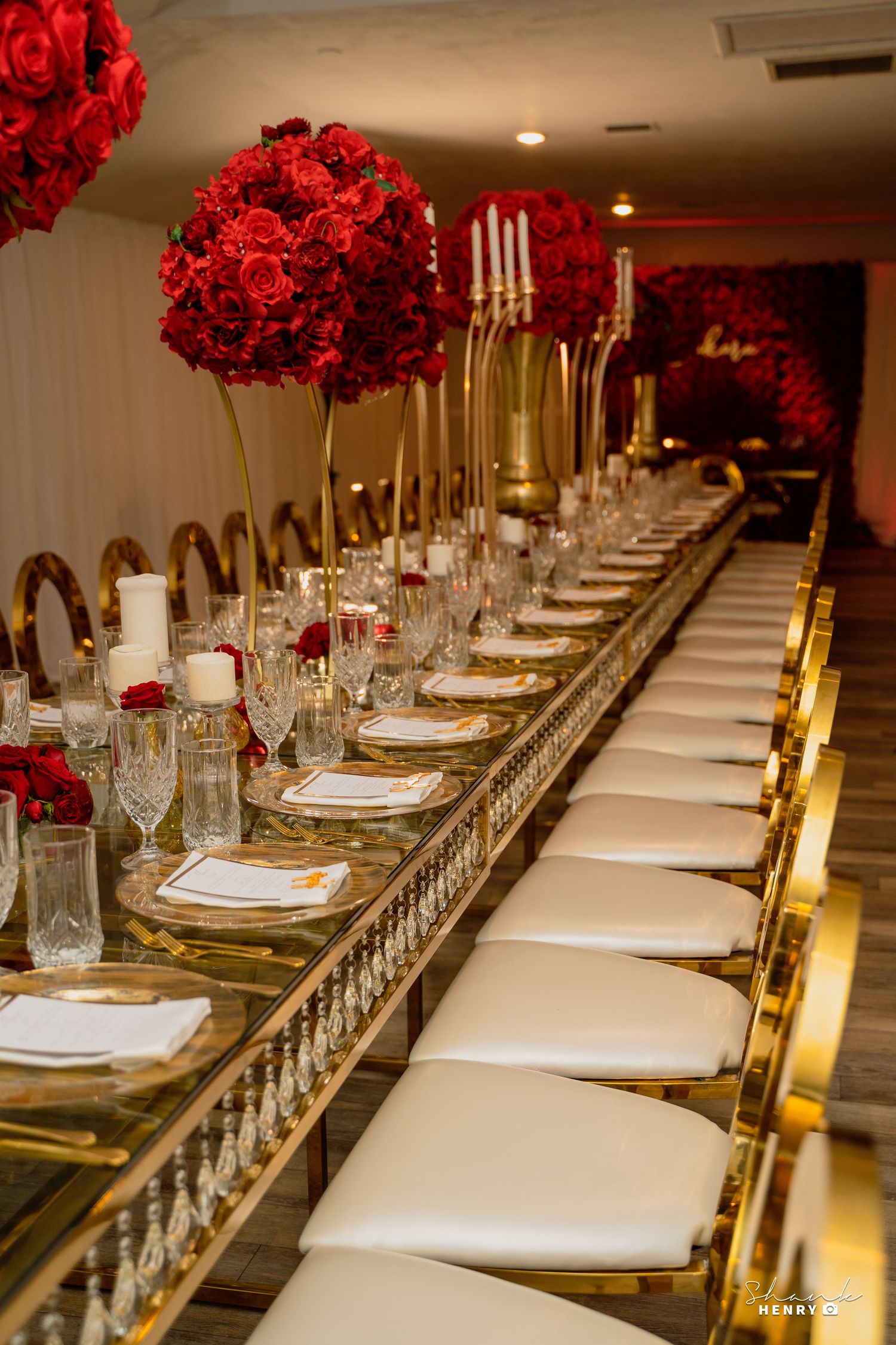 Elegant table setting with red rose centerpieces, gold chairs, and white place settings.