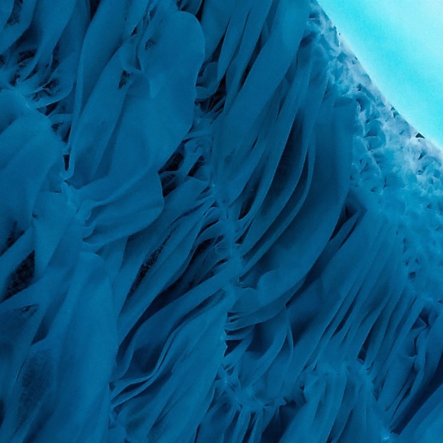 Dramatic ice formation with vertical blue ridges creating a layered wall-like structure.