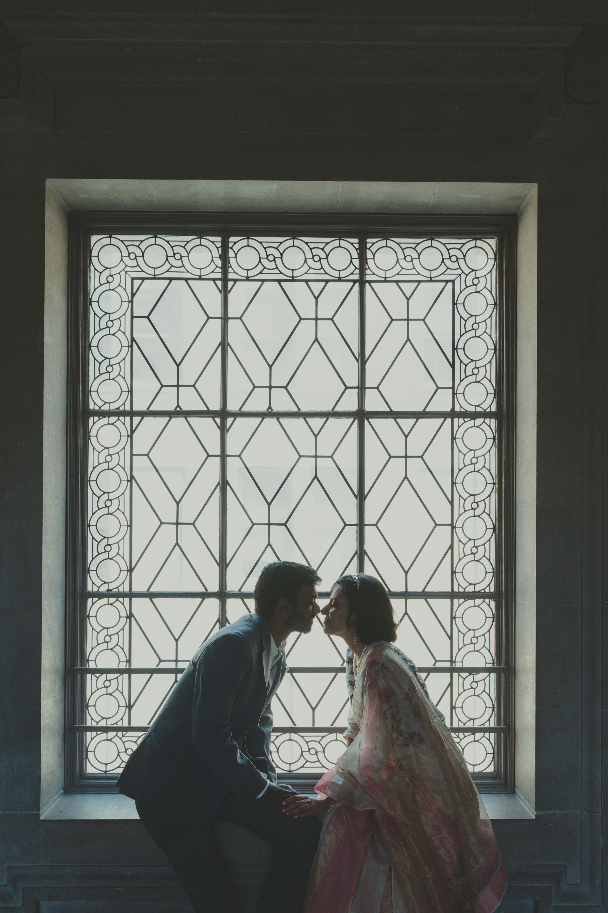 Silhouette of a couple about to kiss in front of an ornate stained glass window.