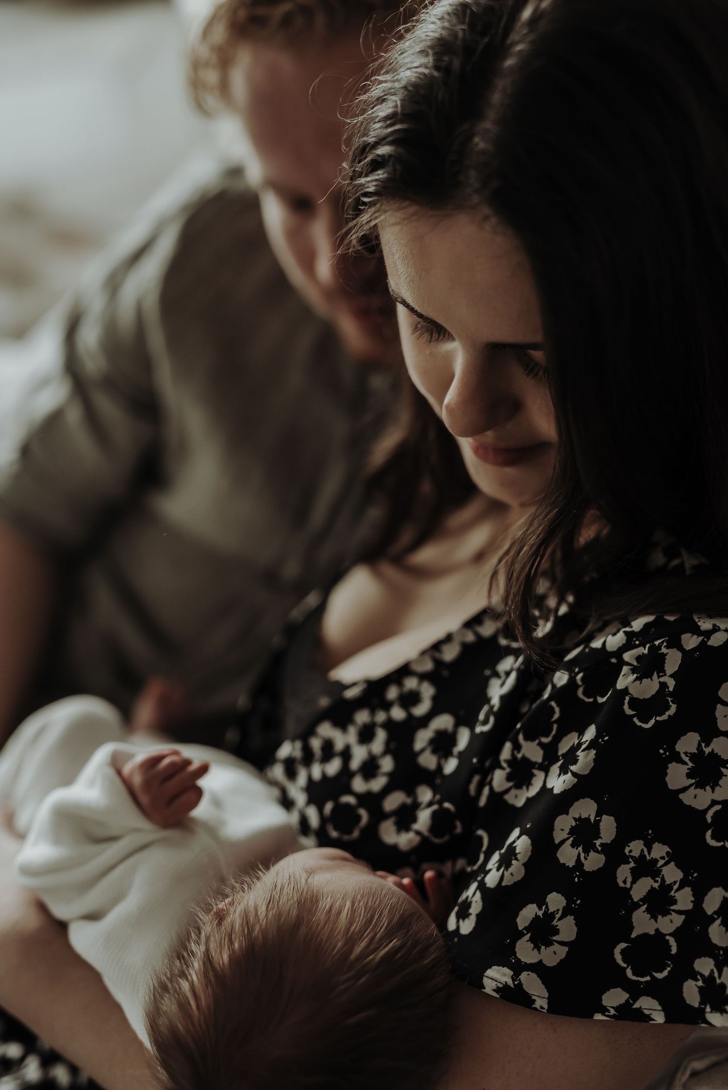Intimate moment between parent and newborn baby in moody lighting.