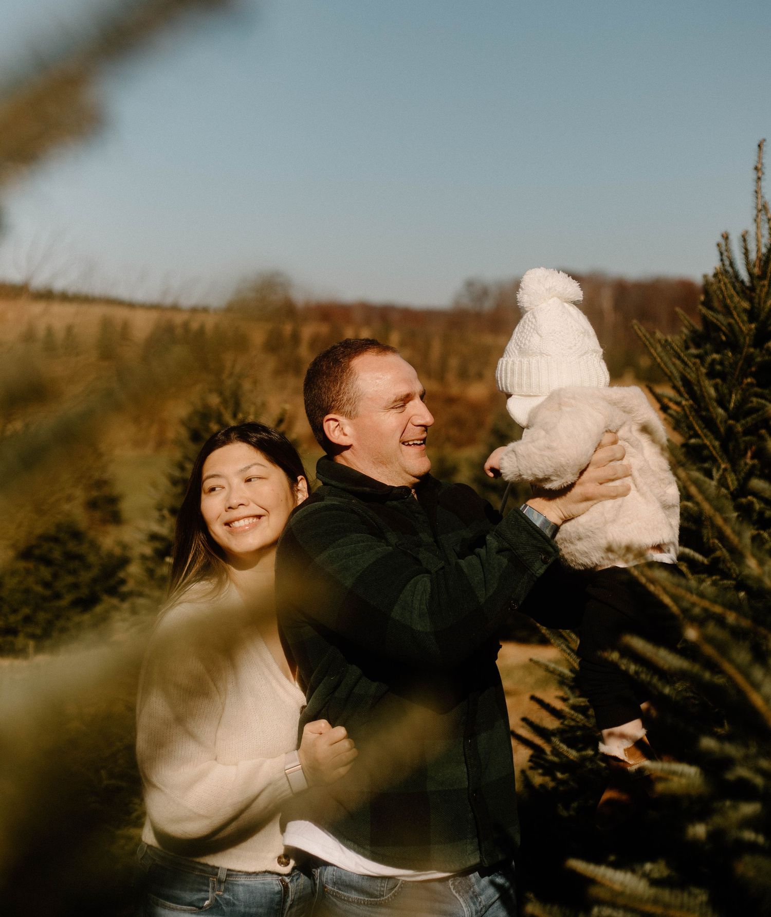 Family shares joyful moment among evergreen trees at Christmas tree farm.