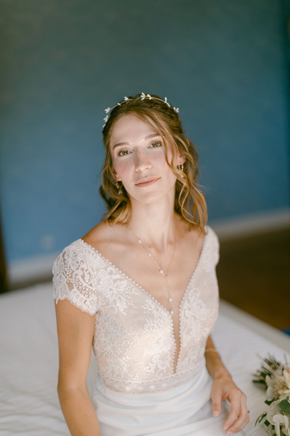 Portrait d’une personne portant une délicate robe de mariée en dentelle avec des manches courtes, sur un fond bleu.