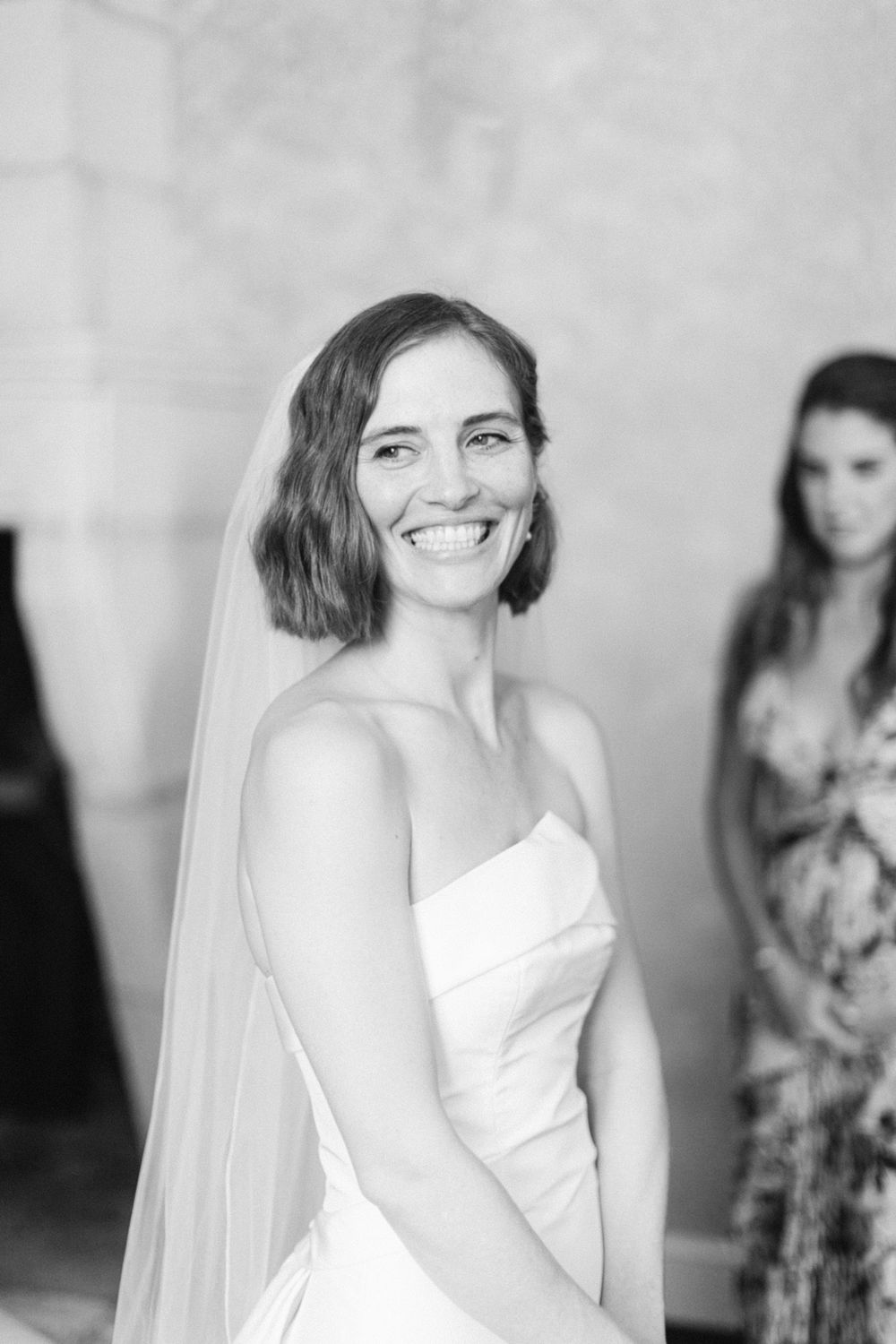 Portrait en noir et blanc d’une personne portant une robe de mariée sans bretelles et un voile flottant.