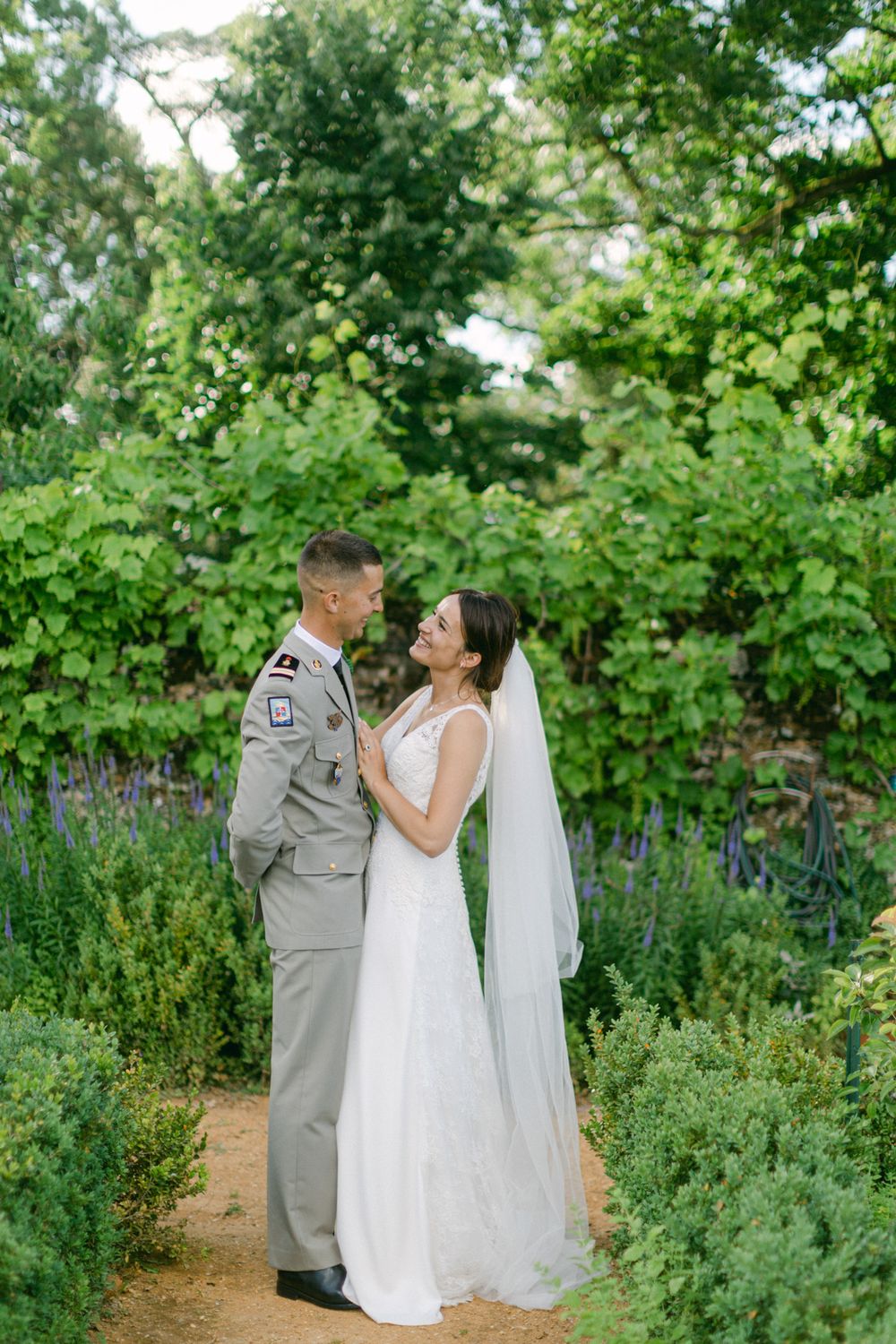 Le couple de mariés s’enlace dans un jardin luxuriant, entouré de lavande en fleurs et de verdure.