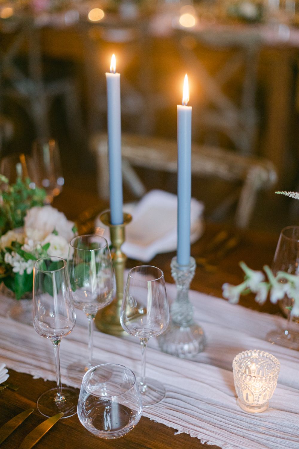 Table élégante décorée de bougies blanches hautes, de verres en cristal et de délicates compositions florales.