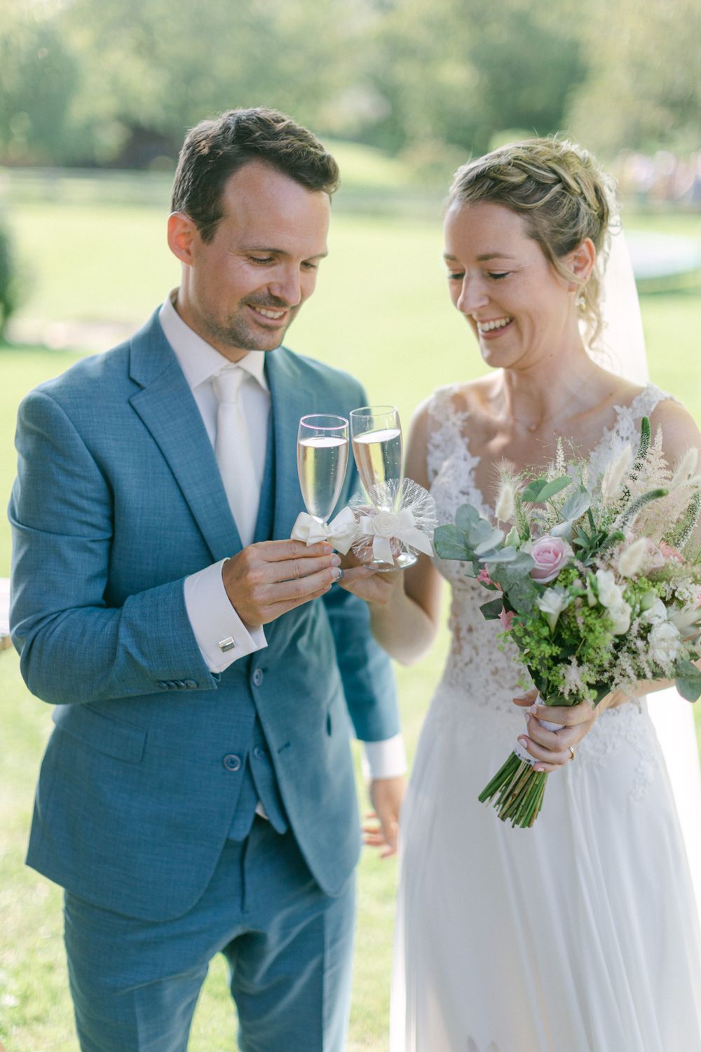 Le couple de mariés porte un toast avec du champagne en plein air tout en tenant le bouquet.