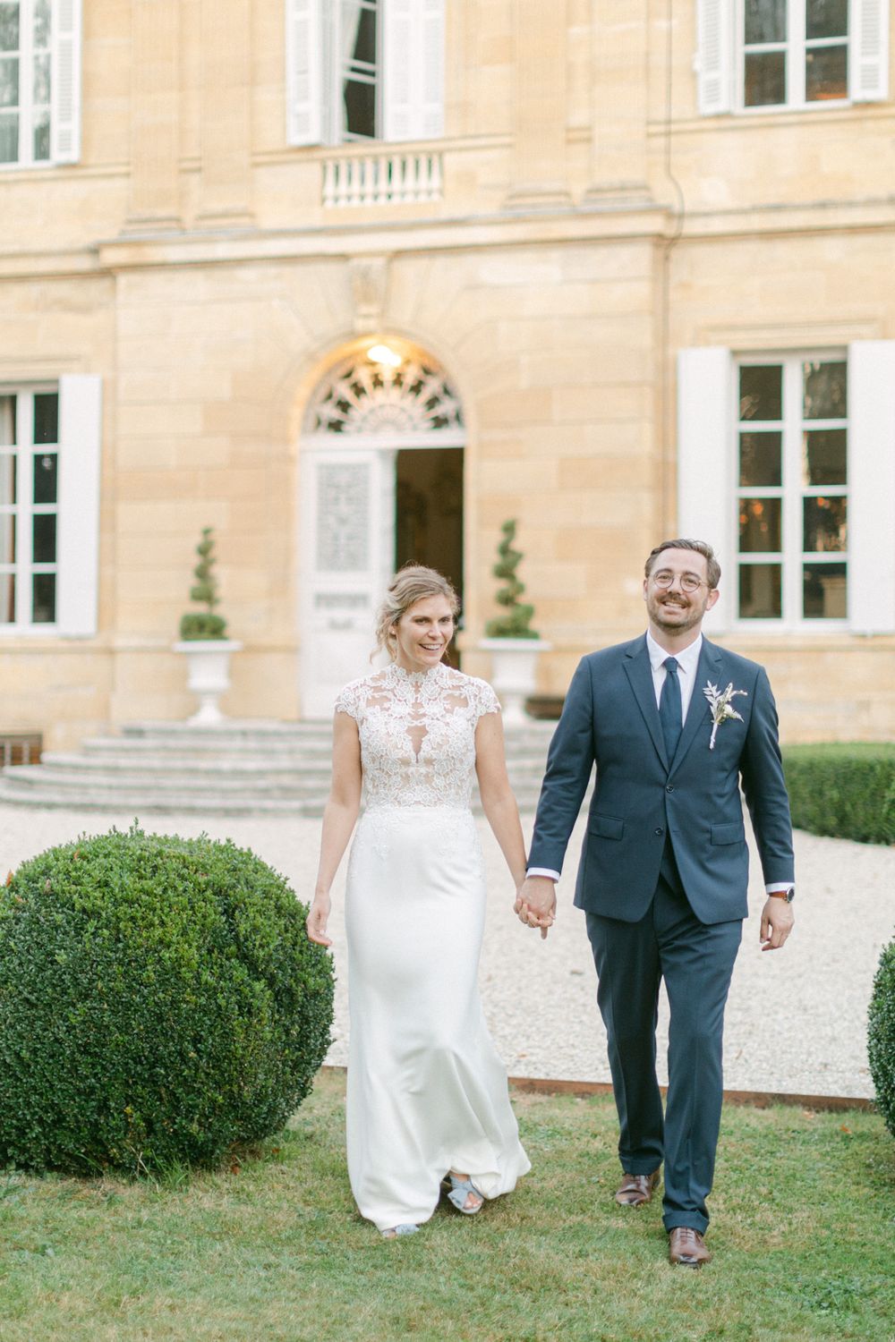 Le couple marche ensemble à l’extérieur d’un élégant manoir de style français, entouré de jardins bien entretenus.