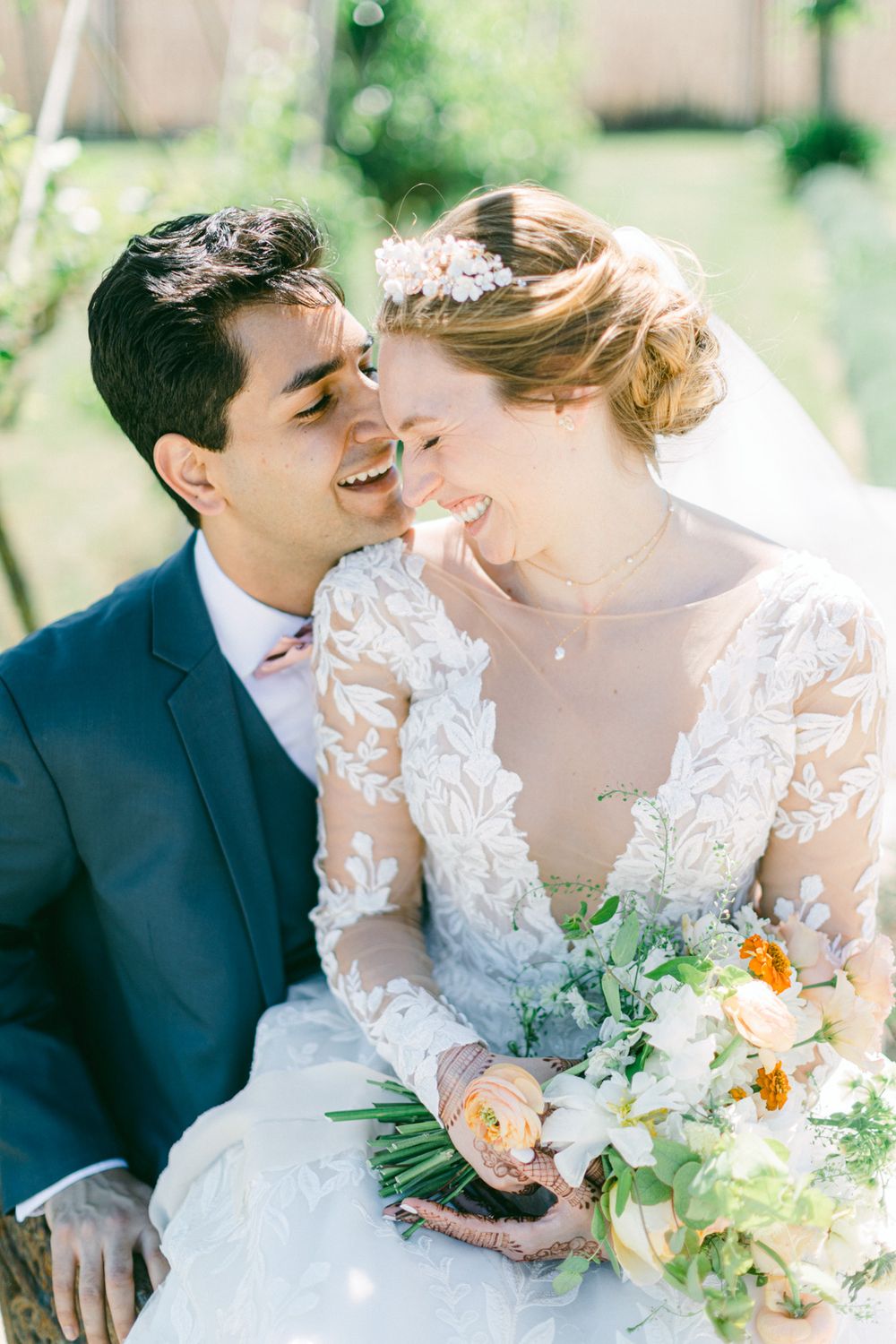 Le couple partage un moment joyeux, la mariée tenant un bouquet pastel dans un cadre en plein air.