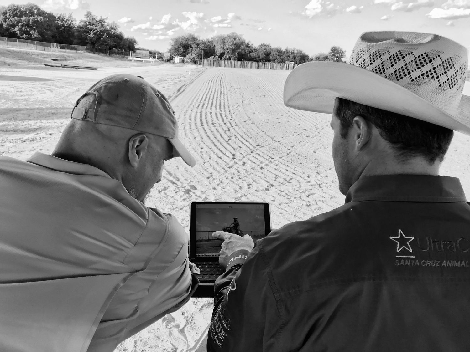 Two people in cowboy hats review content on a tablet device in an outdoor setting.