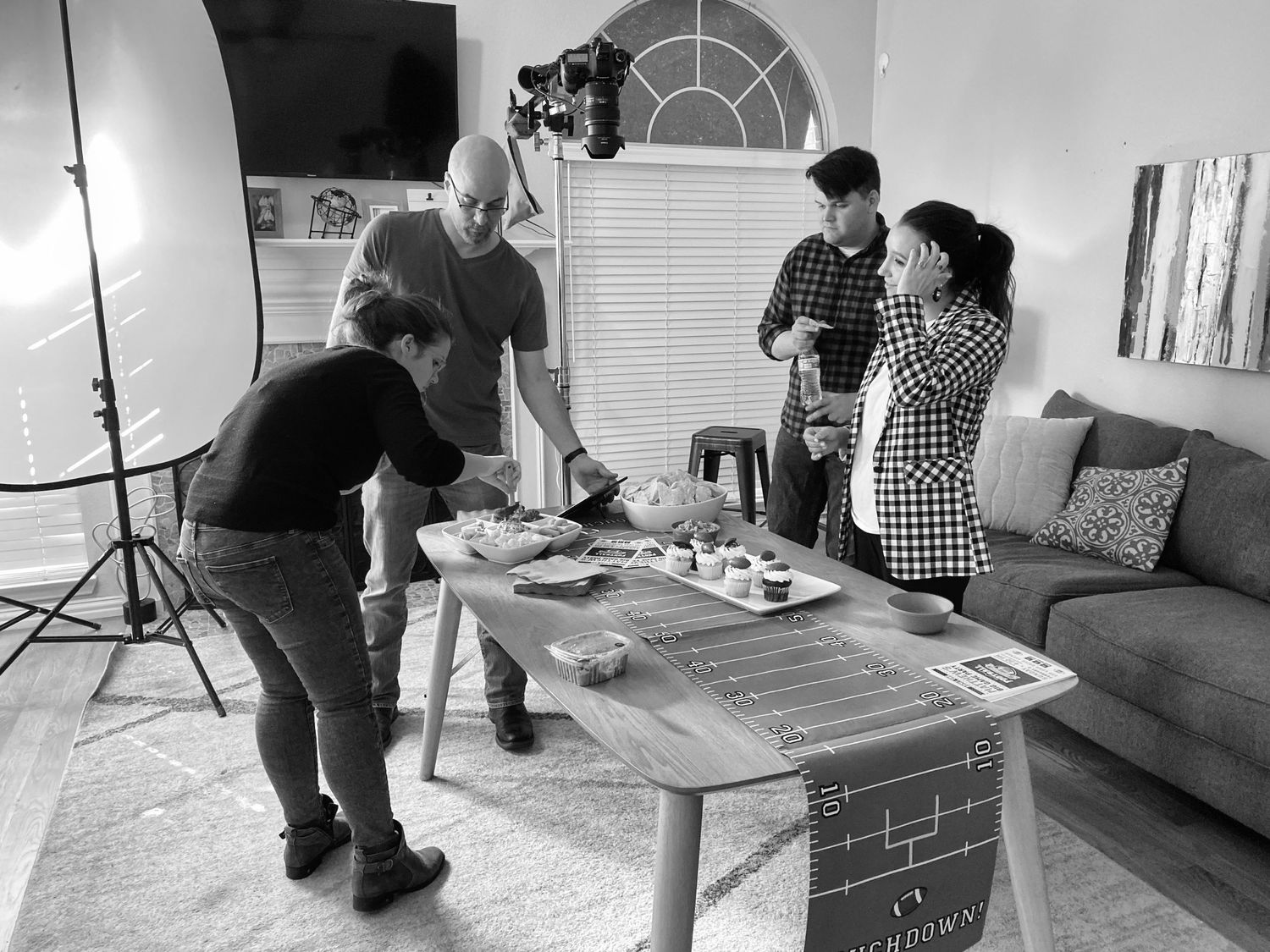 Film crew setting up equipment and props for food photography shoot in living room.