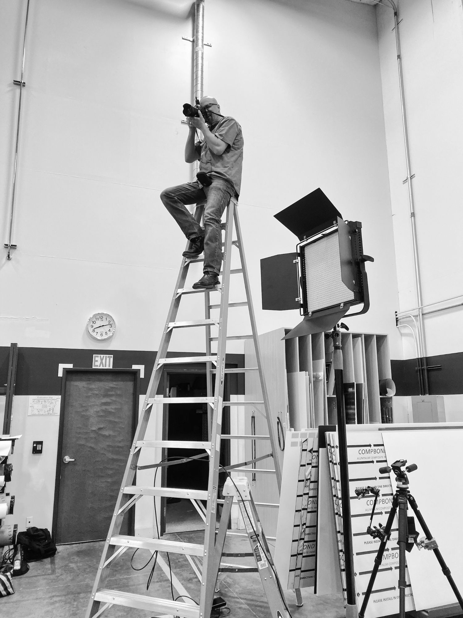 Camera operator climbing ladder to adjust lighting equipment in studio space.