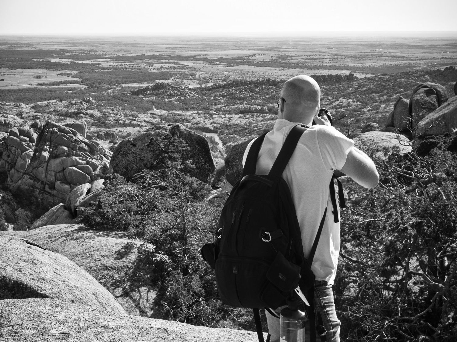 Person with backpack overlooking scenic mountain landscape from rocky viewpoint.