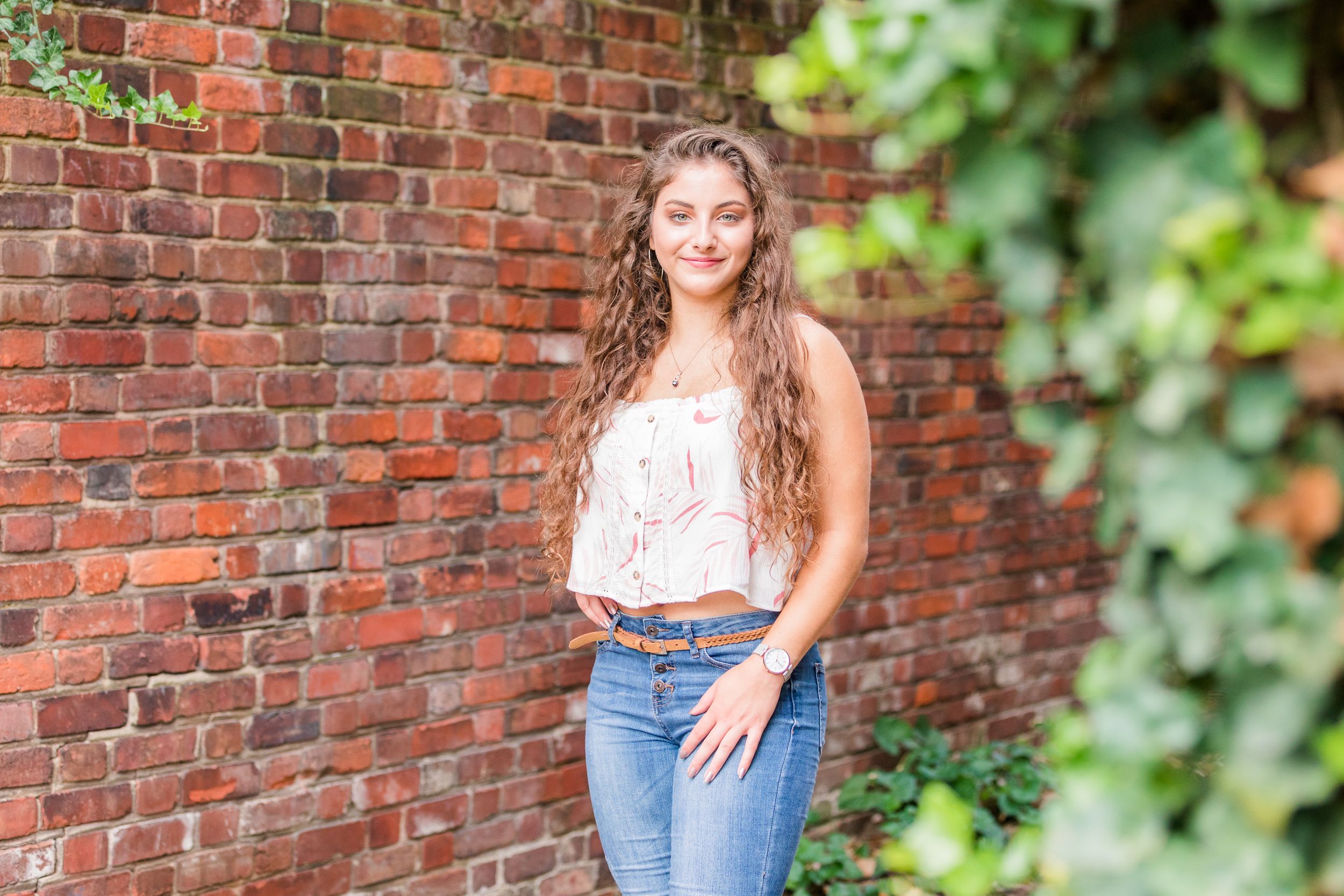Senior girl posing in brick alley with ivy in foreground