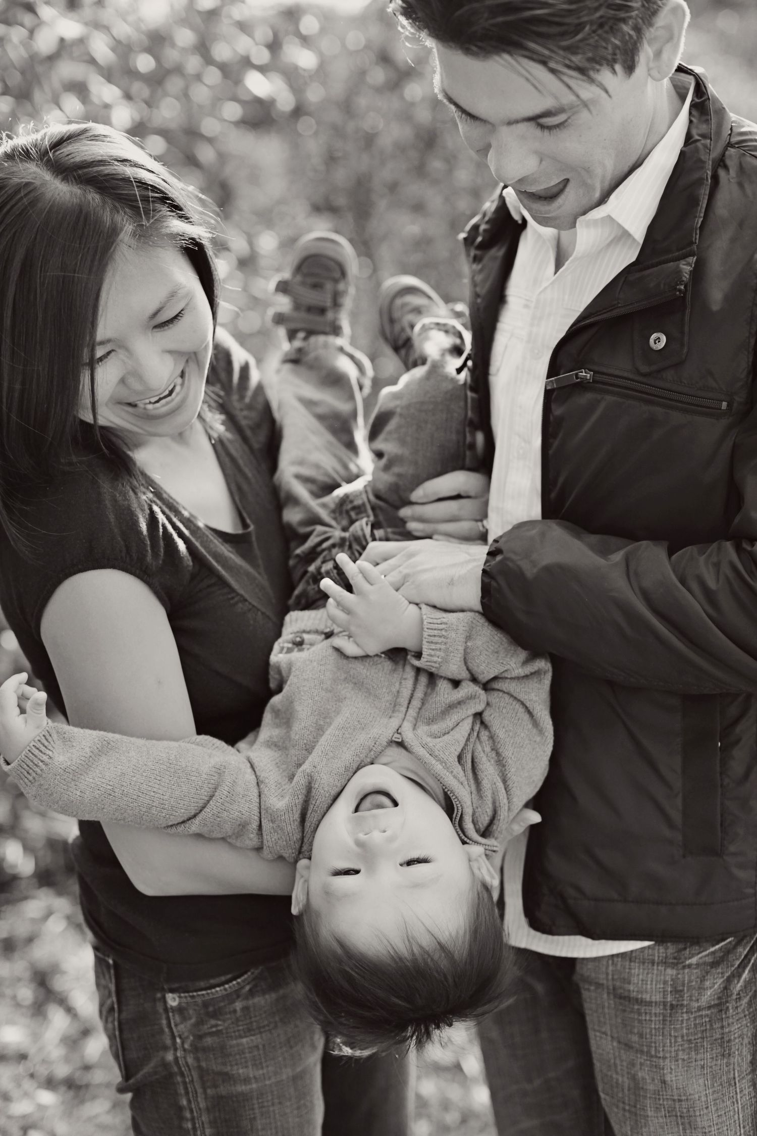 Family playing together outdoors in black and white photo, holding child upside down playfully.