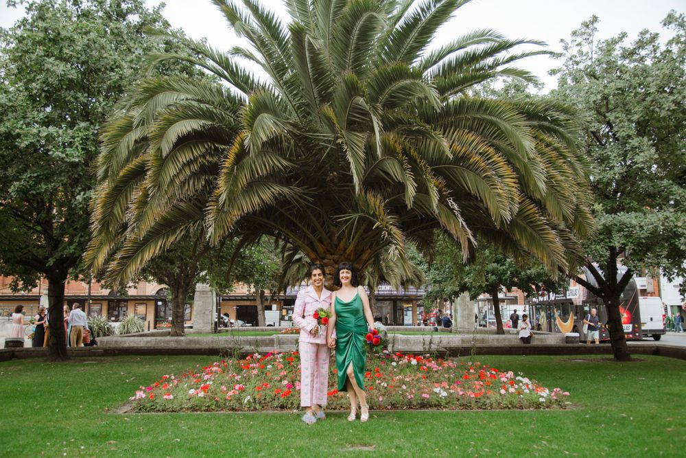 Couple poses in front of large palm tree and flower garden.
