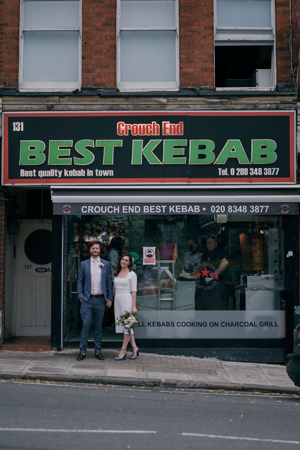 A couple poses outside Best Kebab restaurant storefront on a city street.