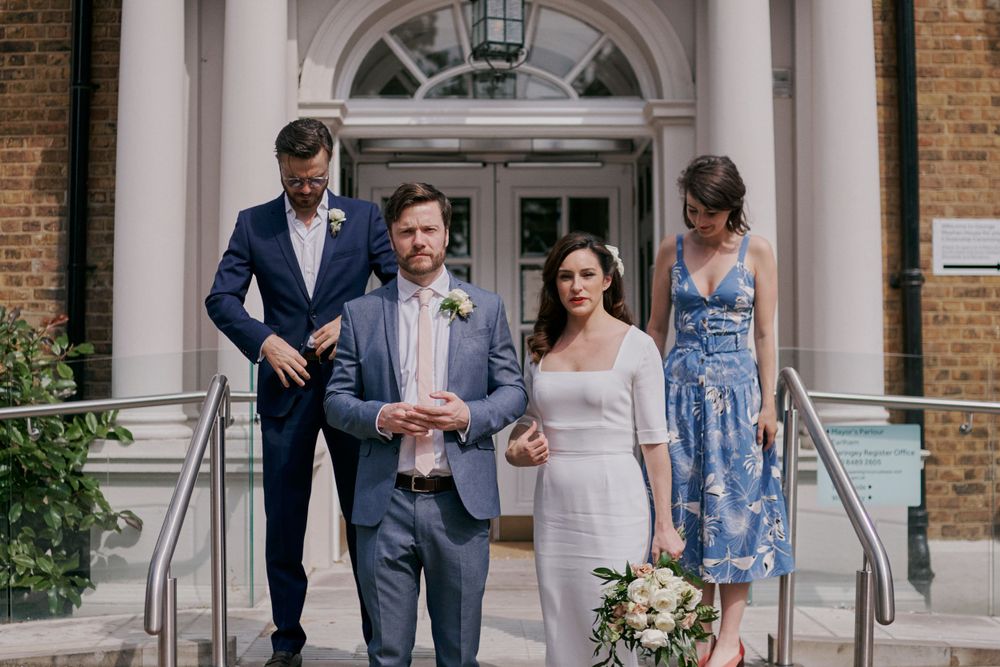 A wedding party poses together on the steps of a historic building with brick and white columns.