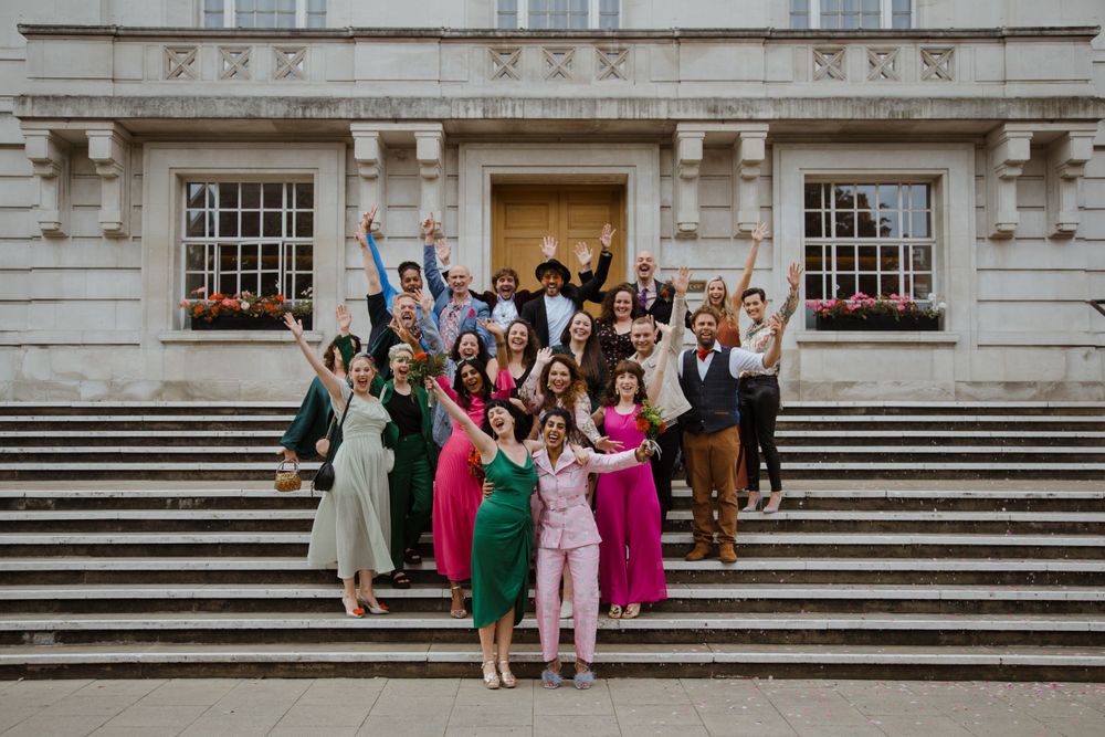 Large wedding party poses on grand stone steps of historic building.
