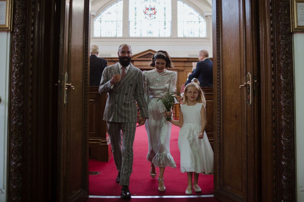 A joyful group walks down a pink-carpeted church aisle after a wedding ceremony.