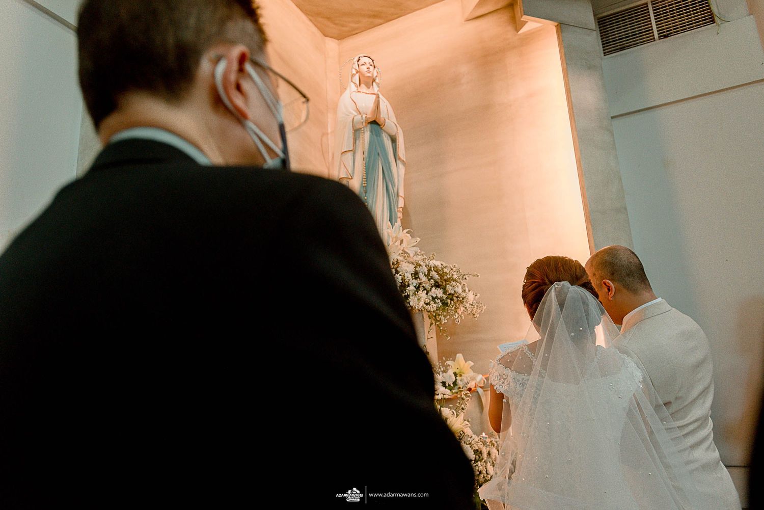A couple stands before a religious statue during their wedding ceremony.