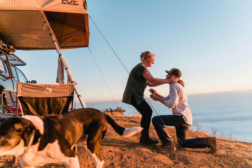 Couple and dog share special moment at scenic overlook with rooftop tent camping setup.