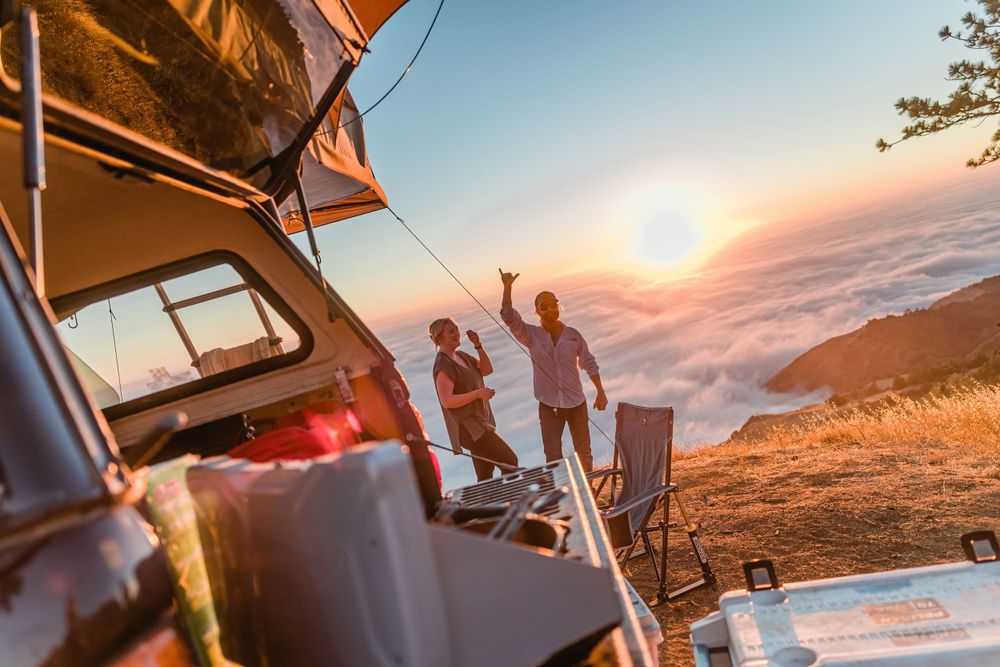 Adventurers celebrating sunset from their rooftop tent campsite high above the clouds.