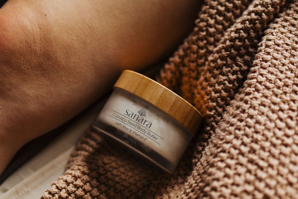 Close-up of Sanara beauty cream jar with wooden lid on knitted blanket.