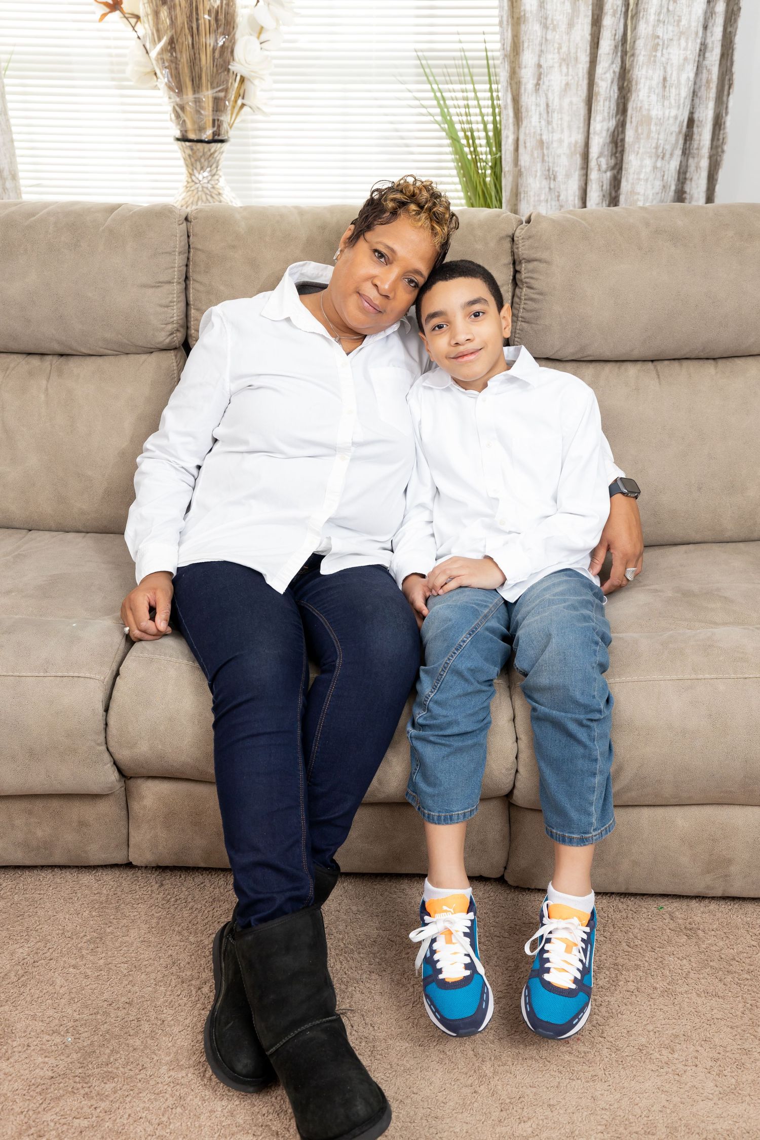 Parent and child sitting close together on a beige couch wearing white and blue casual clothing.