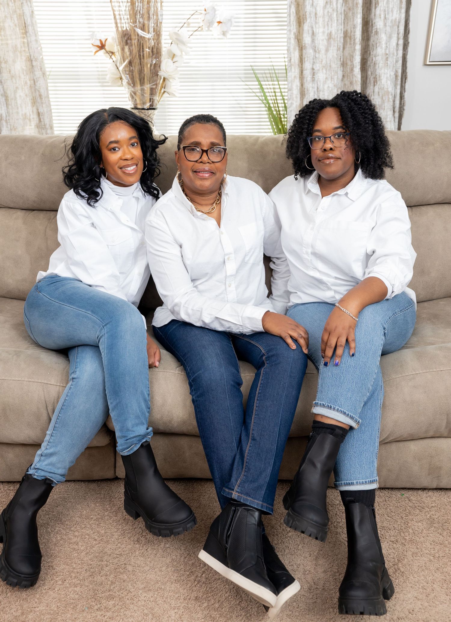 Three people in matching white button-down shirts and jeans pose casually on a beige sofa.